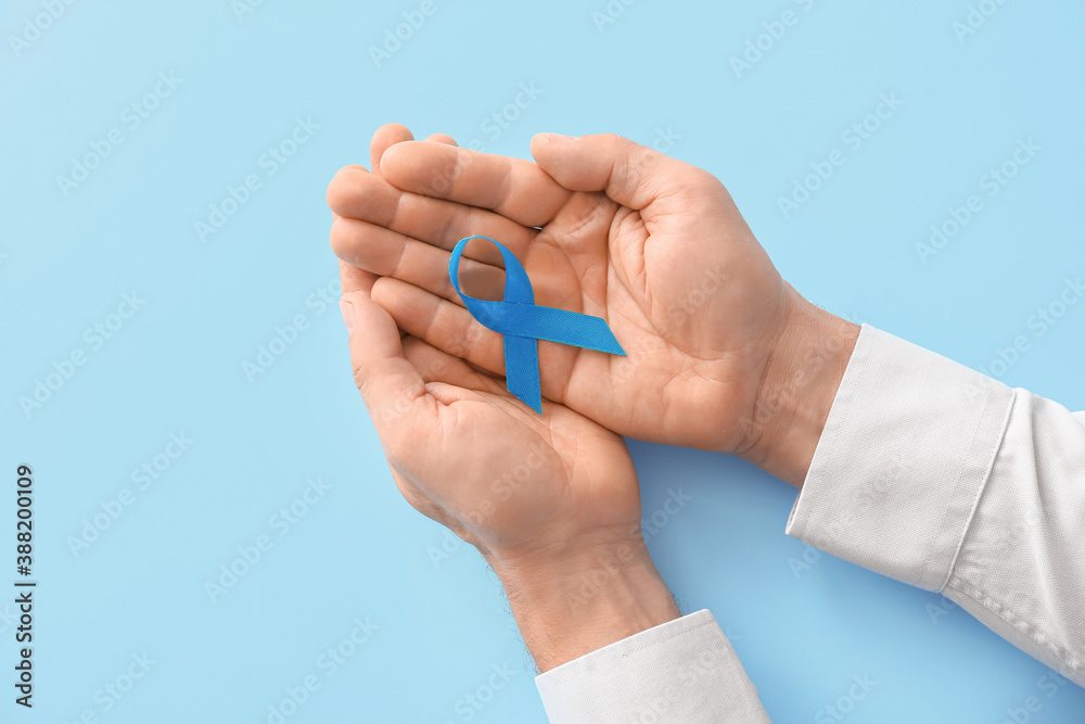 Male hands with blue ribbon on color background. Prostate cancer awareness concept - obrazy, fototapety, plakaty 