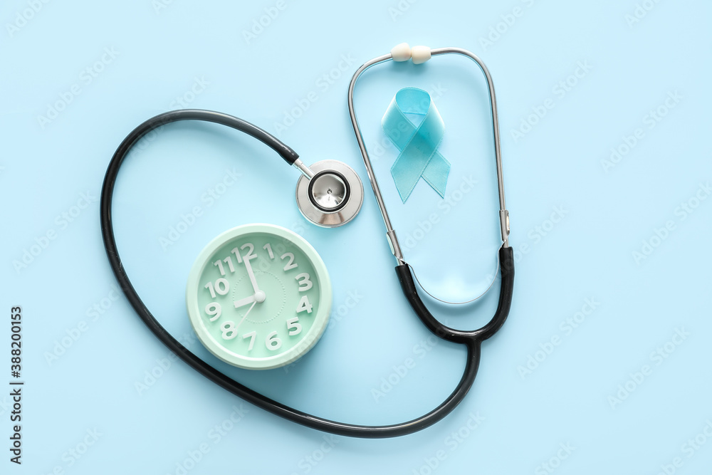 Blue ribbon, alarm clock and stethoscope on color background. Prostate cancer awareness concept