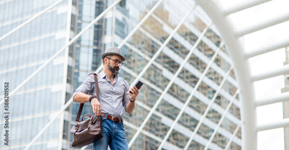 Caucasian man tourist walking in the city using smartphone with internet for navigation map or online message. Beard guy carry leather bag using application on mobile phone call a cab in the city.