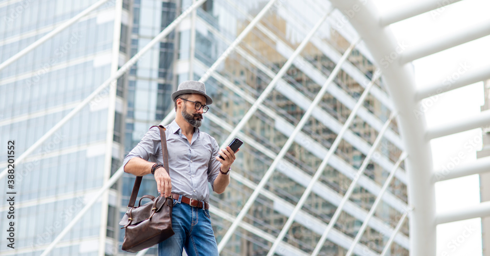 Caucasian man tourist walking in the city using smartphone with internet for navigation map or online message. Beard guy carry leather bag using application on mobile phone call a cab in the city. Caucasian man tourist walking in the city using smartphone with internet for navigation map or online message. Beard guy carry leather bag using application on mobile phone call a cab in the city.