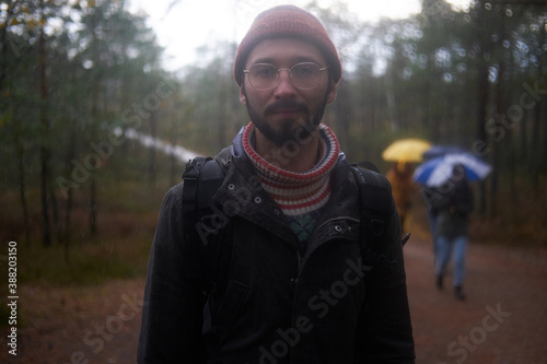 Contrast and dark photography of bearded guy with backpack and glasses he stay with sun behind him in autumn forest.