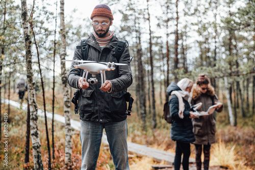 Lovely and relaxed autumn forest and bearded guy he holds quadcopter and two girls they stay behind. © Fxquadro