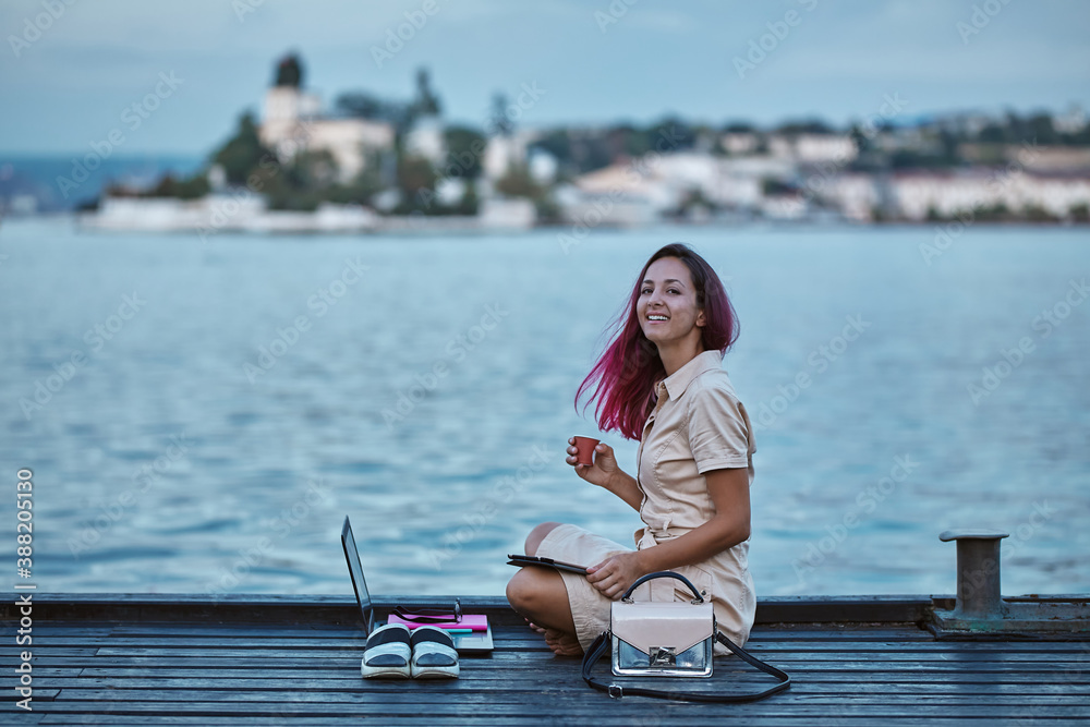 Cheerful woman drinking coffee studying on pier. Laptop and notebook for study. Studentship and distance learning idea