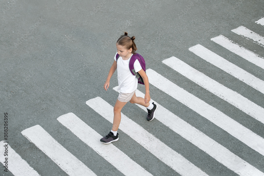 Schoolgirl crossing road on way to school. Zebra traffic walk way in the city. Concept pedestrians passing a crosswalk.  Stylish young teen girl walking with backpack. Active child. Top view