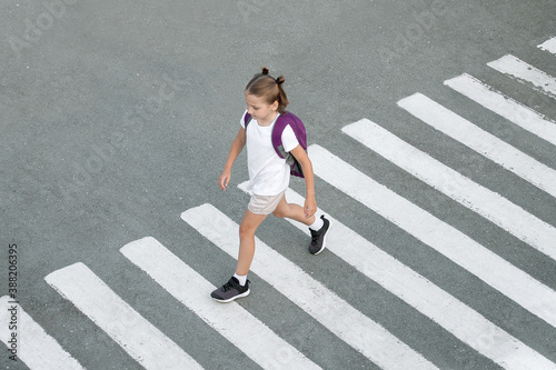 Schoolgirl crossing road on way to school. Zebra traffic walk way in the city. Concept pedestrians passing a crosswalk.  Stylish young teen girl walking with backpack. Active child. Top view