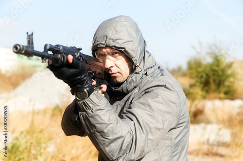 man in a jacket with a hood aims at the gun, outside