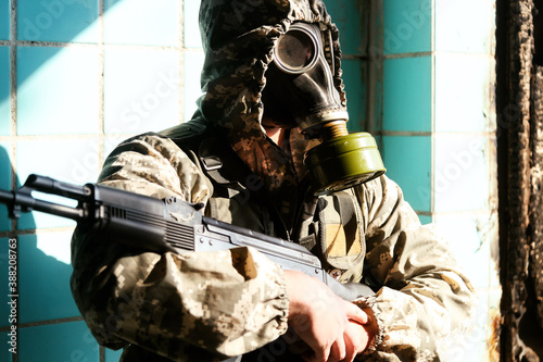 military man in a gas mask, hooded, holding a weapon in his hands, stands at the window of the destroyed building
