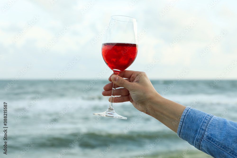 Female hand hold glass of wine against sea