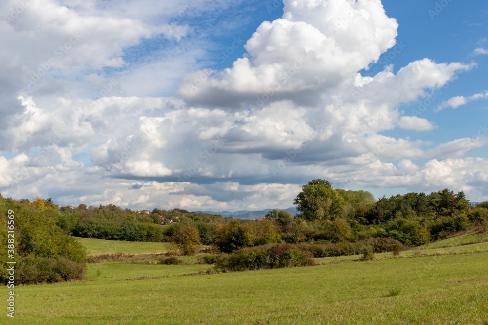 Autumn landscape, a magnificent sky with white cumulus clouds hanging over a hilly regiment with bushes and trees
