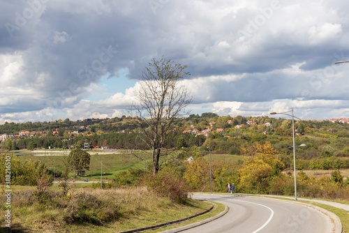 Autumn landscape, view from the hill across the road to the city district with private houses, orange roofs among the trees