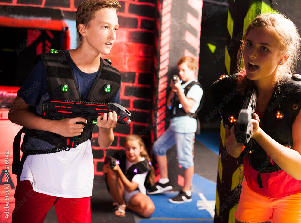 Excited teen kids aiming laser guns at other players during lasertag game in dark room..