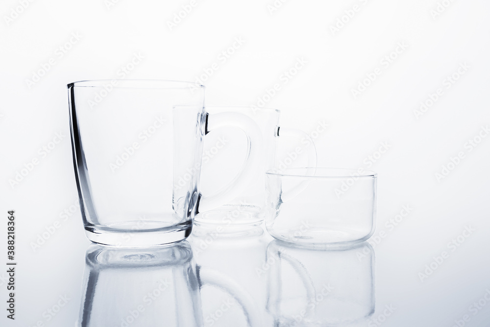 Two empty transparent glass mugs and saucer rosette on reflective surface on white background. Black and white transparent glass still life. Two empty transparent glass mugs and saucer rosette on reflective surface on white background. Black and white transparent glass still life.