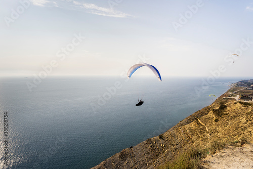 A paraglider flies over mountains and sea in a blue sky on a Sunny summer day.