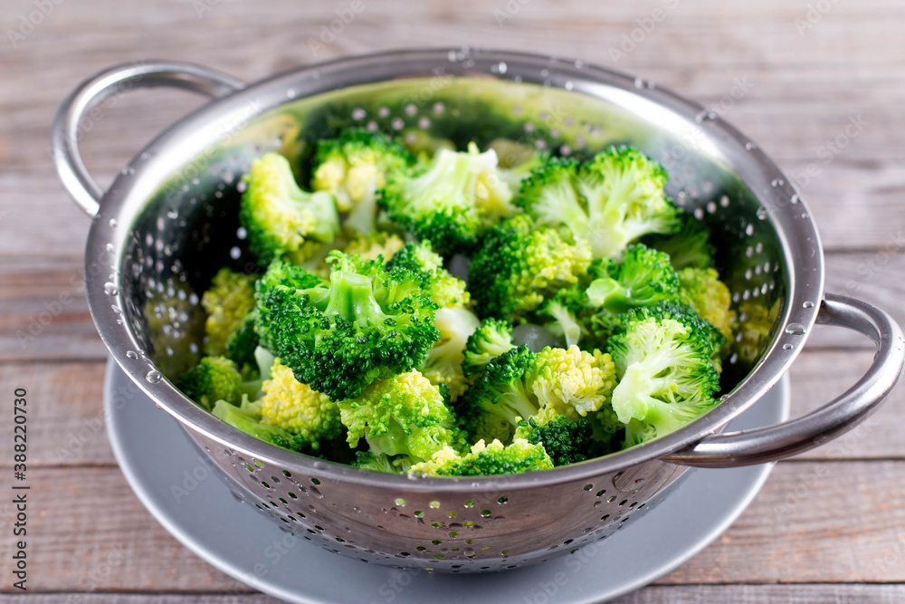 Blanched broccoli in colander on a wooden background. Healthy diet. Colander with fresh green broccoli on table Blanched broccoli in colander on a wooden background. Healthy diet. Colander with fresh green broccoli on table