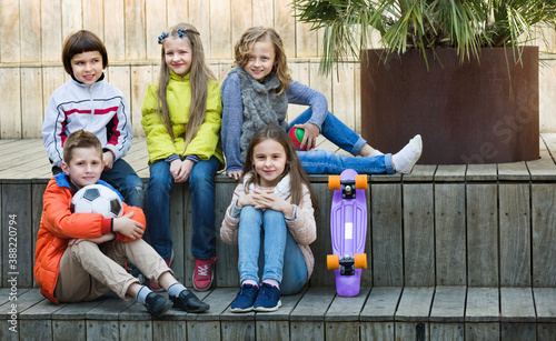 Group of ordinary cheerful smiling children portrait with ball and skateboard outdoors © JackF