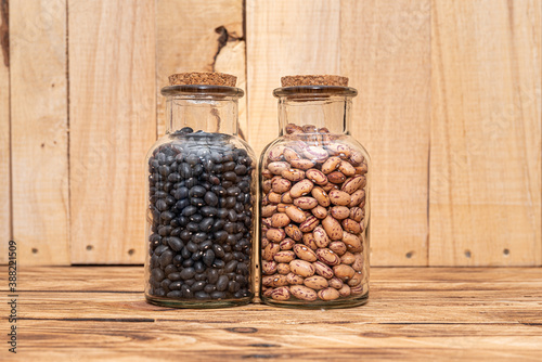 Two jars of dried beans. Black Beans and Borlotti Beans, dried for preservation and long term storage on natural wooden background.