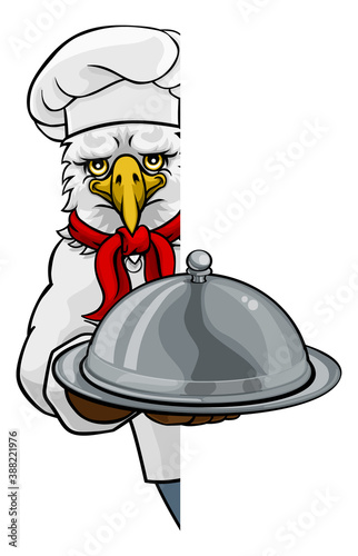 An eagle chef mascot cartoon character holding a silver platter cloche dome of food peeking round a sign
