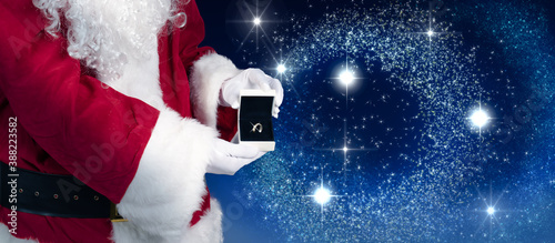 Santa is holding a jewelry case with a ring as a Christmas present in his hand