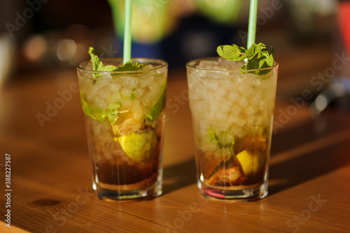 Two glasses of mojito cocktail with fresh lime and mint on a wooden table in a bar or nightclub