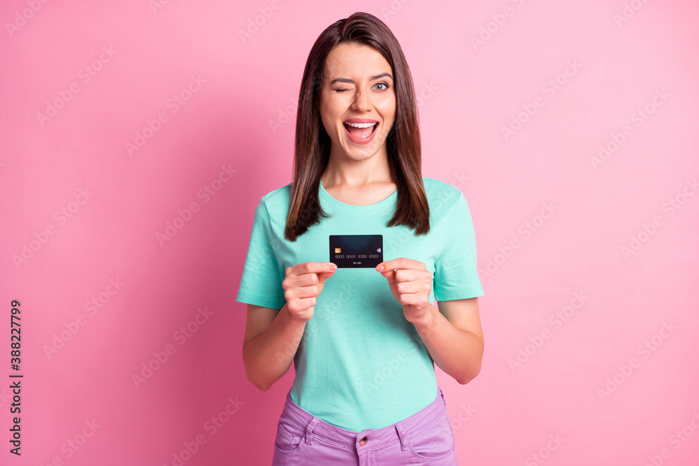 Photo portrait of woman holding credit card in two hands winking isolated on pastel pink colored background - obrazy, fototapety, plakaty 