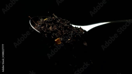 Full spoon of leaf tea. Black helbal floral leaf tea falling from spoon in slow motion isolated on black background. Healthy eating, hot energy healthy drinks, nutrition, harm benefits of tea concept