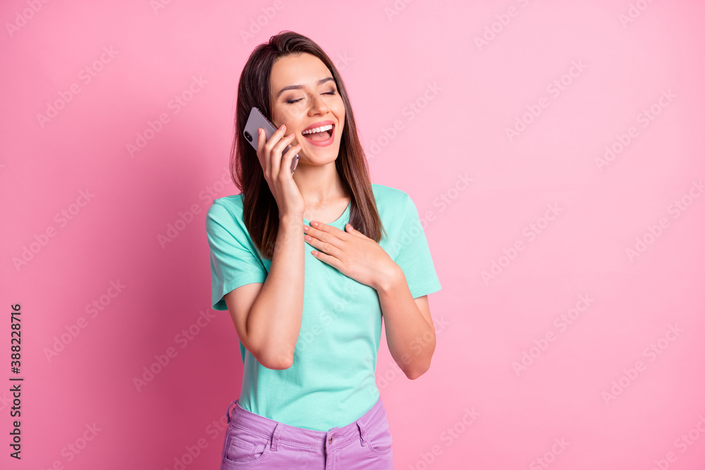 Photo portrait of laughing girl touching chest with one hand talking on phone isolated on pastel pink colored background Photo portrait of laughing girl touching chest with one hand talking on phone isolated on pastel pink colored background