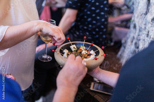Person taking a skewer from the skewer plate of fresh cheese, salmon and spices tapas in a wooden bowl. Ideal tapas for corporate events, weddings, baptisms, communions.