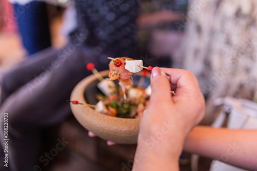 Person taking a skewer from the skewer plate of fresh cheese, salmon and spices tapas in a wooden bowl. Ideal tapas for corporate events, weddings, baptisms, communions.
