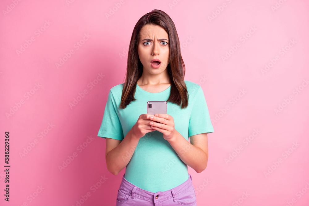 Photo portrait of upset woman holding phone in two hands isolated on pastel pink colored background Photo portrait of upset woman holding phone in two hands isolated on pastel pink colored background