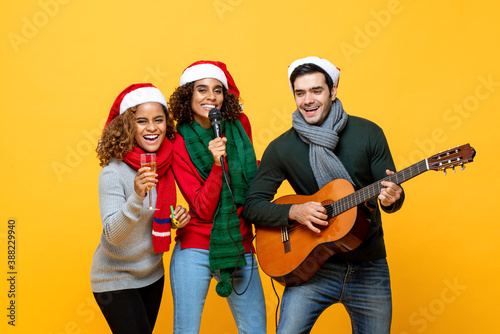Joyful diverse friends having party singing drinking and celebrating Christmas on yellow isolated background