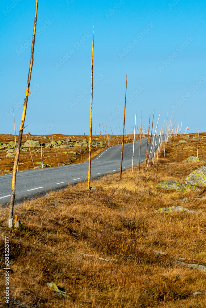 Asphalt road through the mountain highlands, with tall wooden marking sticks placed on the side. Blurred background. Asphalt road through the mountain highlands, with tall wooden marking sticks placed on the side. Blurred background.