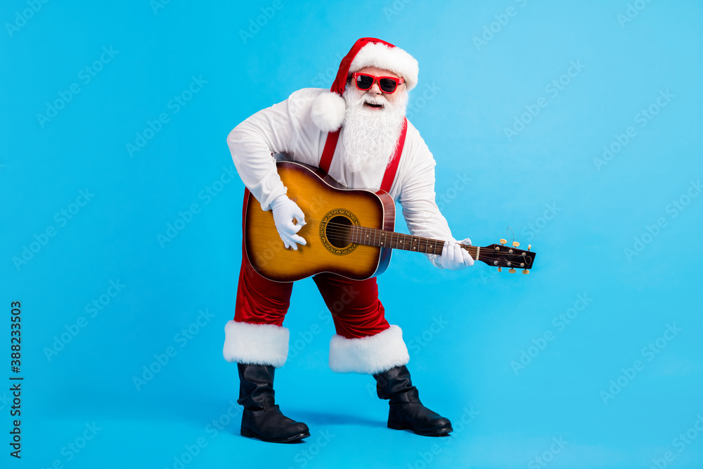 Full body photo of crazy funky pop star santa claus with big beard stomach play guitar instrument on x-mas christmas spirit event wear suspenders overall cap isolated blue color background Full body photo of crazy funky pop star santa claus with big beard stomach play guitar instrument on x-mas christmas spirit event wear suspenders overall cap isolated blue color background