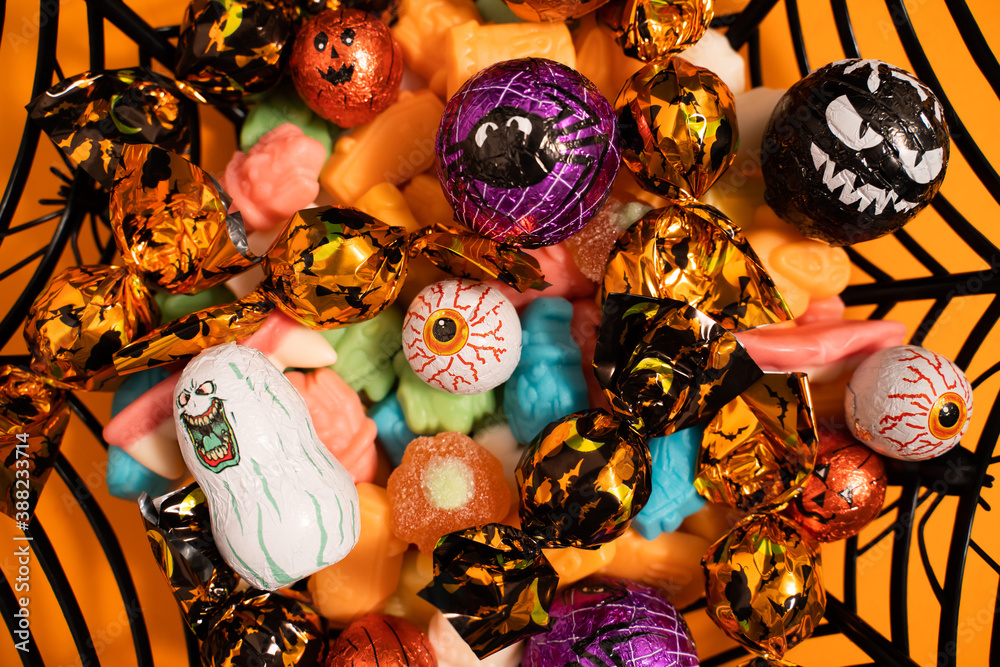 Funny Halloween candy of different colors in a bowl shaped like a black spider web on an orange background. Close up.