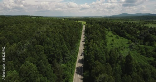 One dark car driving alone / travel on empty straight asphalt road freeway through dense forest corridor at summer sunny day. Aerial drone wide view. photo