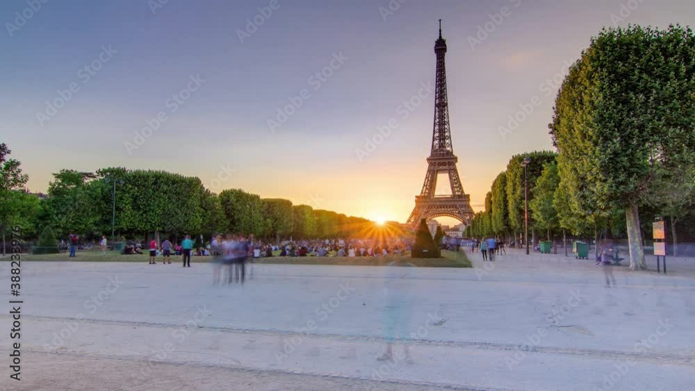 Eiffel Tower seen from Champ de Mars during sunset timelapse, Paris, France. People sitting on lawn and walking around. Summer evening with clear sky