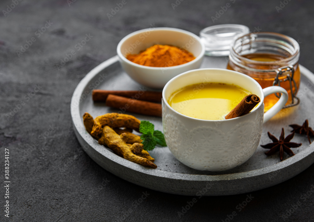 Yellow turmeric latte drink. Golden milk with cinnamon, turmeric, ginger and honey over black concrete background. Yellow turmeric latte drink. Golden milk with cinnamon, turmeric, ginger and honey over black concrete background.