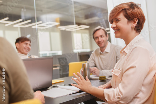 Female entrepreneur laughing, talking to her creative team during meeting at the office