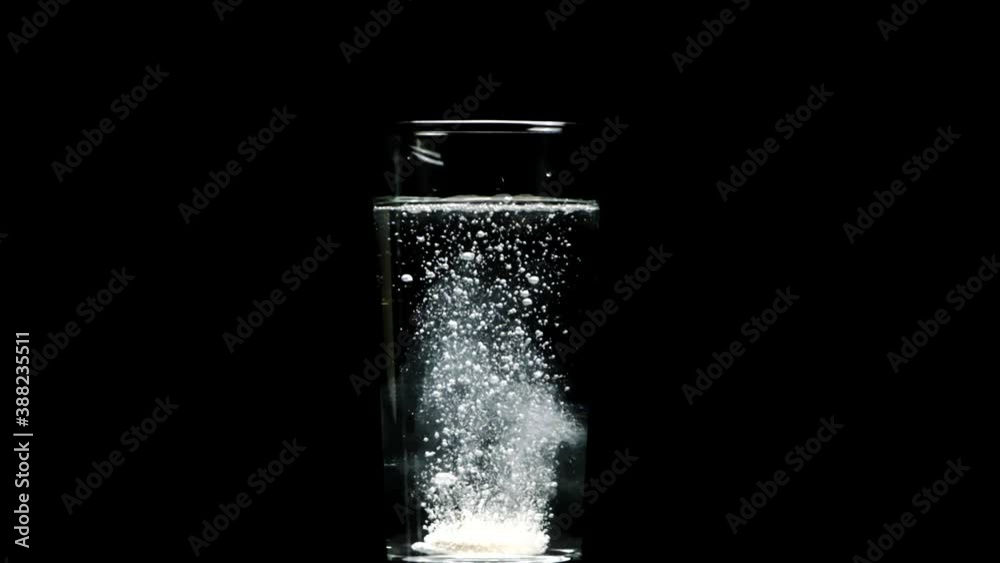 Effervescent or carbon tablet dissolves with bubbles in transparent glass with pure water, slow motion, isolated black background. Vitamins C pills against flu, medicines, aid, energy concept