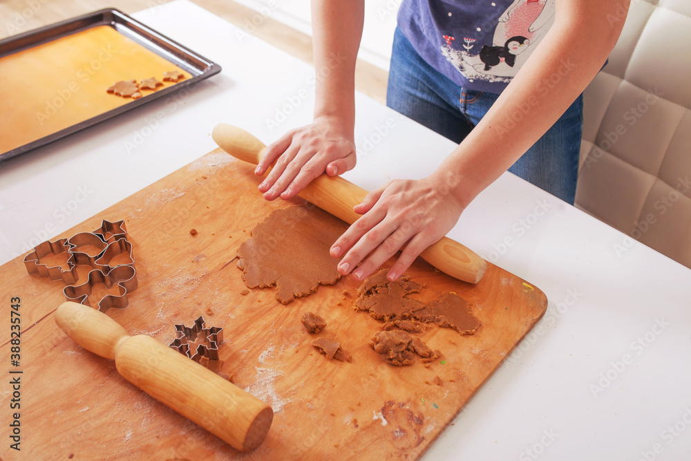 Christmas baking. Teenager's hands making cookies. Ginger dough for gingerbread, gingerbread men, stars, Christmas trees, rolling pin, flour. On the home kitchen white table. Christmas baking. Teenager's hands making cookies. Ginger dough for gingerbread, gingerbread men, stars, Christmas trees, rolling pin, flour. On the home kitchen white table.