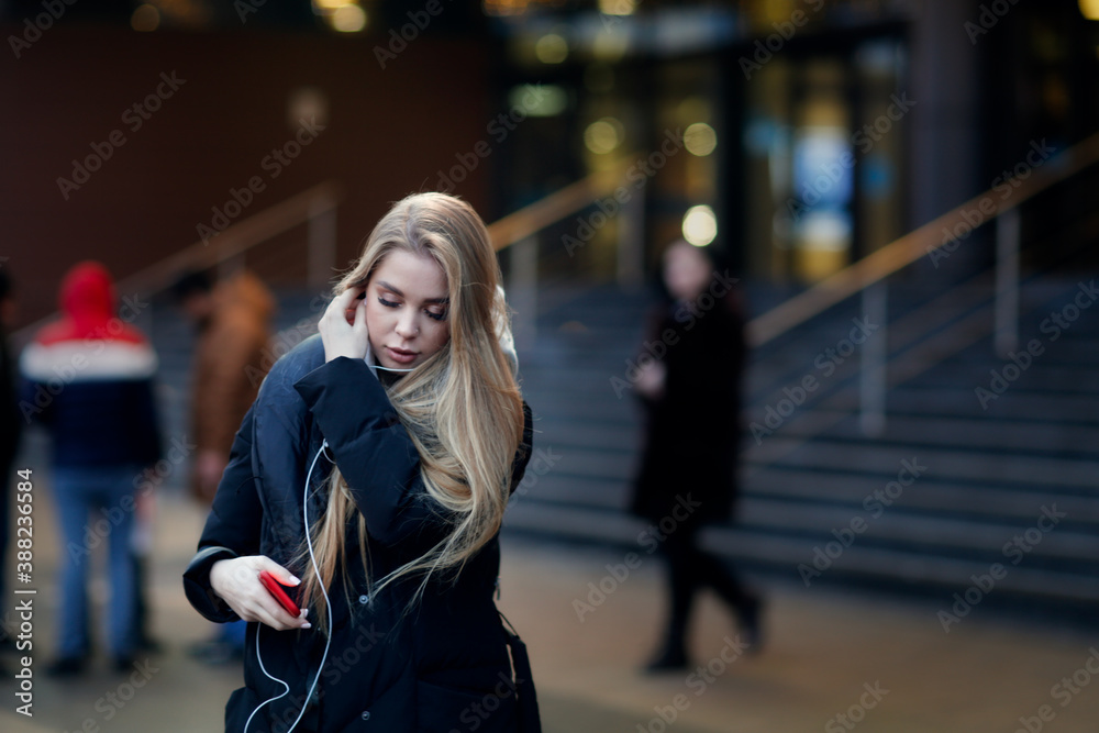 Fototapeta premium Caucasian girl woman in a long down coat in the city with a phone, the concept of safety and life in the city, communication