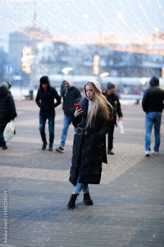 Caucasian girl woman in a long down coat in the city with a phone, the concept of safety and life in the city, communication