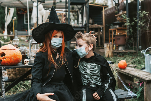 a boy in a skeleton costume and a girl in a witch costume wearing a protective face mask at a Halloween party in a new reality due to the covid pandemic