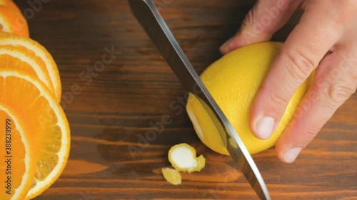 Male hand with big knife slicing lemon citrus fruit on the cutting board at kitchen. cooking process in home, top view