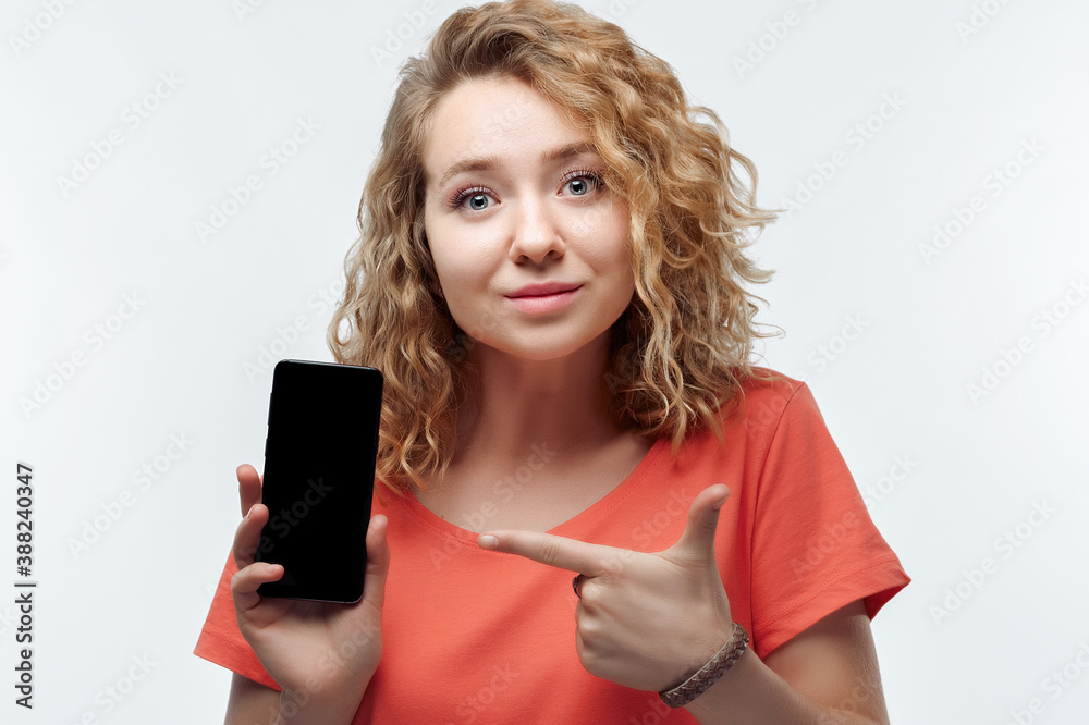 Naklejka premium Young woman Showing Smartphone Blank Screen, looking at Camera Recommending Mobile App