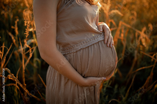 Pregnant young blonde woman with long hair at sunset. Hands and belly close up.