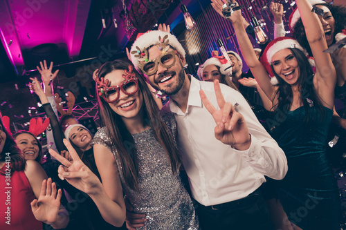 Photo of funky lovely people man cuddle lovely girl shiny smile show v-sign deer x-mas specs modern club indoors