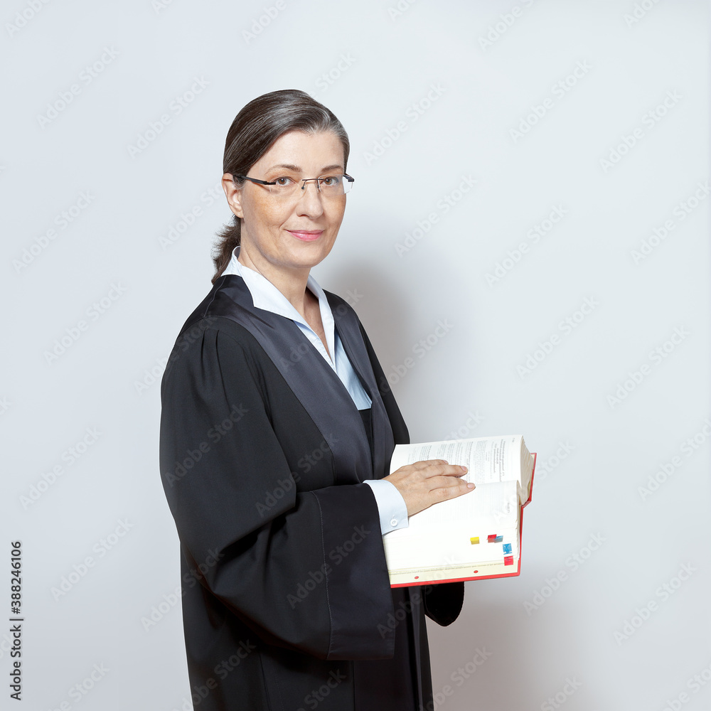 Female lawyer concept: portrait of an middle aged woman in a black gown holding a legislative text book. Female lawyer concept: portrait of an middle aged woman in a black gown holding a legislative text book.