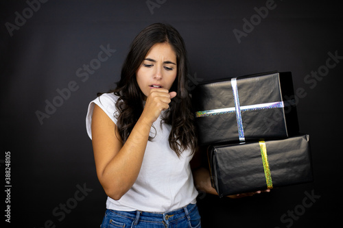 Young beautiful woman holding gifts over isolated black background with her hand to her mouth because she's coughing