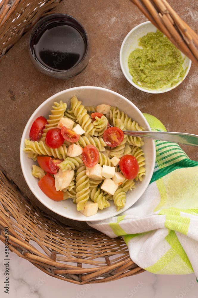 Tomato, mozzarella cheese and arugula pasta salad in a white bowl.