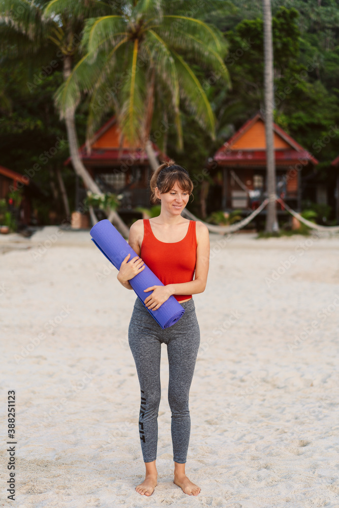 Full length portrait of a smiling sports woman with yoga mat walking